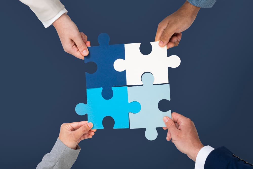Four hands joining pieces of puzzle